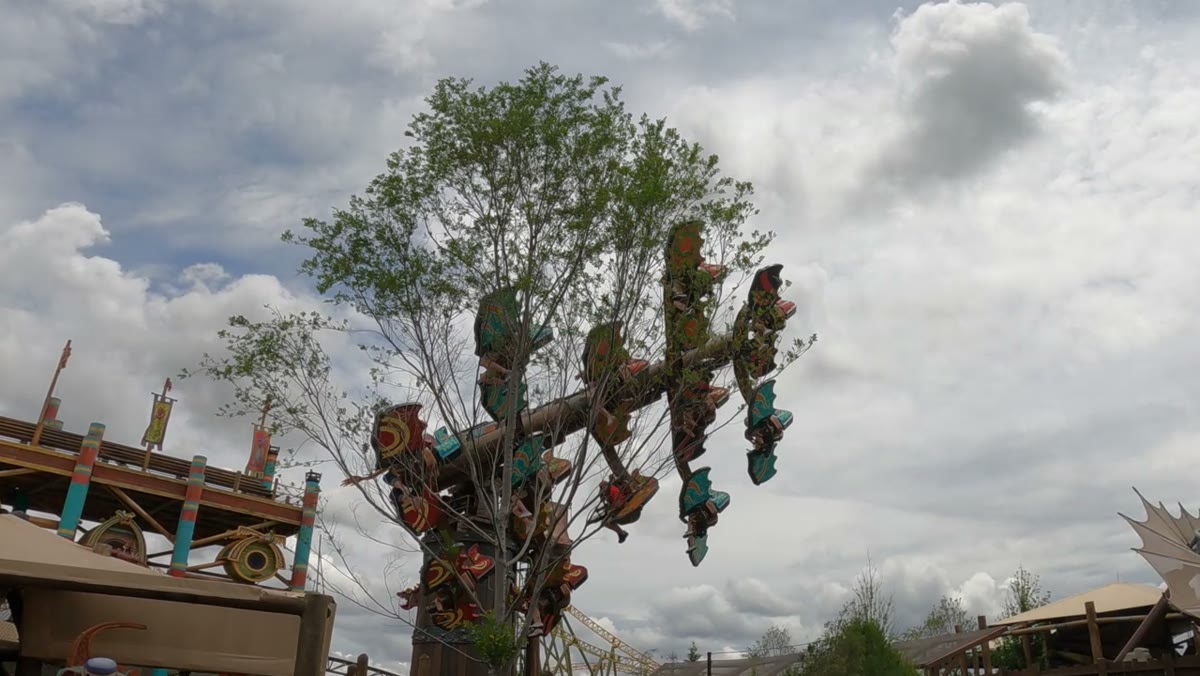 Dragon Racer's Rally in flight at Epic Universe, its arm raised with the dragon ride vehicles in the air, seen from the ground in Isle of Berk