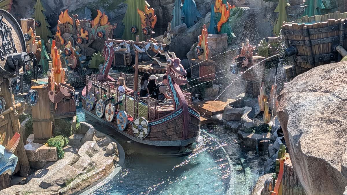 A dragon-headed Viking boat on Fyre Drill at Epic Universe, water cannons firing at flame-painted targets along the canal