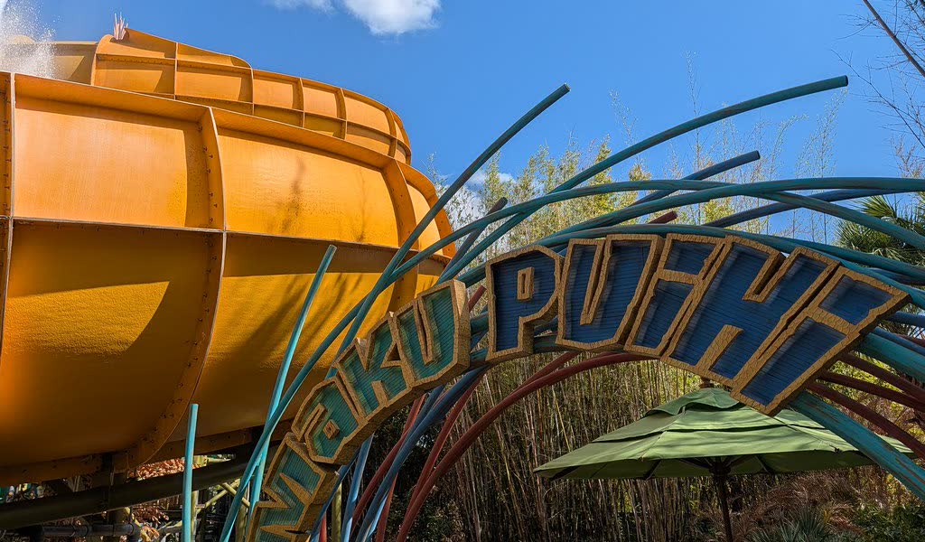 The carved Maku Puihi entrance sign standing beneath the ride’s large orange funnel slide
