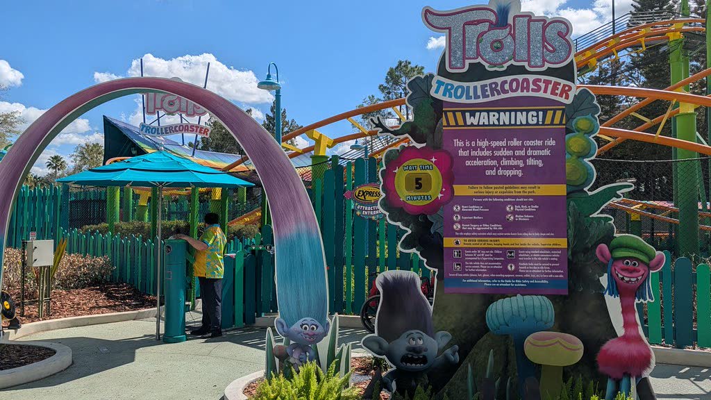 The Trolls Trollercoaster entrance in DreamWorks Land, with its pink and teal archway, troll character figures and the orange coaster track curving behind