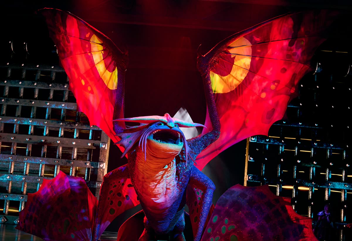 The dragon puppet with wings spread under red stage lighting in The Untrainable Dragon show at Epic Universe